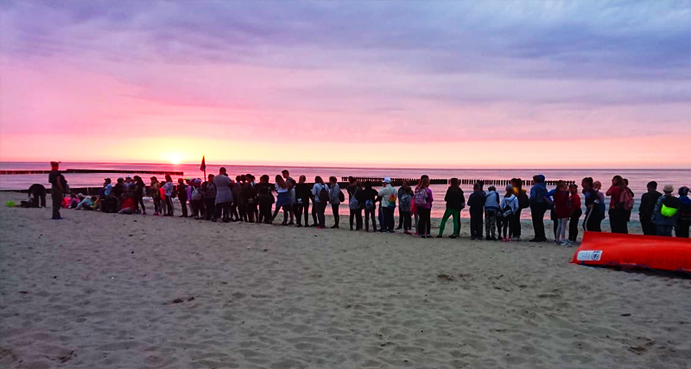 Grupa dzieci na wyjeździe, która stoi na plaży przy zachodzie słońca